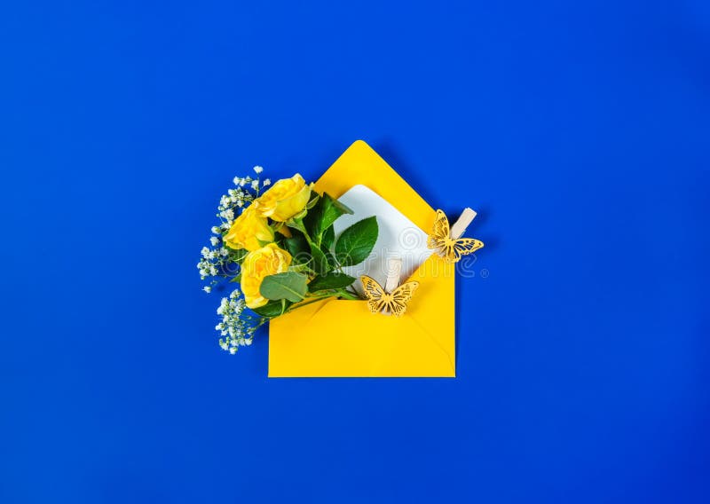 Open envelope with yellow roses, small white filler flowers Gypsophila and yellow butterflies on blue background. Top view, flat lay. Concept of sending greetings, love, friendship and joy. Open envelope with yellow roses, small white filler flowers Gypsophila and yellow butterflies on blue background. Top view, flat lay. Concept of sending greetings, love, friendship and joy.