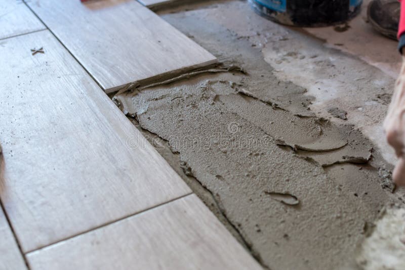 Close up shot of unfinished floor tiles installation in kitchen. Man installing rectangular shaped floor tiles in kitchen. Applying adhesive before installation and verifying afterwards. Close up shot of unfinished floor tiles installation in kitchen. Man installing rectangular shaped floor tiles in kitchen. Applying adhesive before installation and verifying afterwards