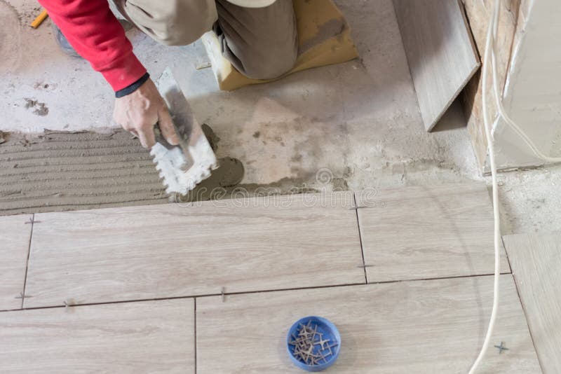 Close up shot of unfinished floor tiles installation in kitchen. Man installing rectangular shaped floor tiles in kitchen. Applying adhesive before installation and verifying afterwards. Close up shot of unfinished floor tiles installation in kitchen. Man installing rectangular shaped floor tiles in kitchen. Applying adhesive before installation and verifying afterwards