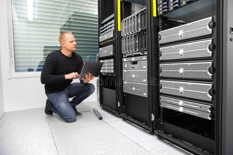Консультант используя компьтер-книжку пока контролирующ серверов в Datacenter стоковое фото Консультант используя компьтер-книжку пока контролирующ серверов в Datacenter стоковое фото