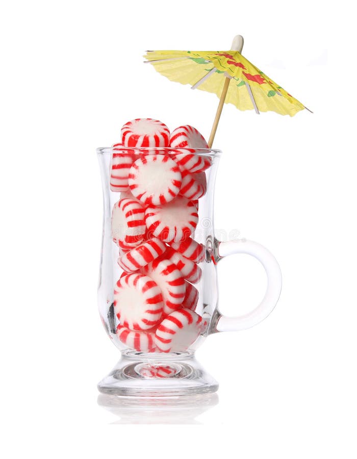 Peppermint candy in glass and cocktail umbrella isolated on white. Concept. Red striped mint Christmas candy, macro. Peppermint candy in glass and cocktail umbrella isolated on white. Concept. Red striped mint Christmas candy, macro.