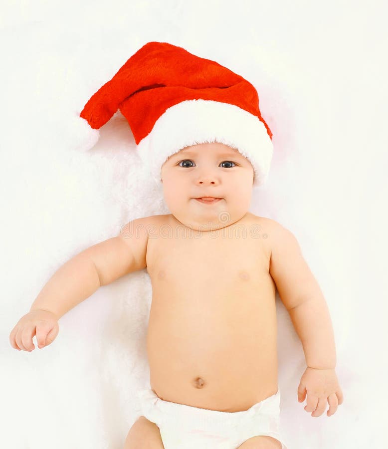 Концепция рождества и семьи - милый младенец в красной шляпе santa лежа на белом доме кровати стоковое фото Концепция рождества и семьи - милый младенец в красной шляпе santa лежа на белом доме кровати стоковое фото