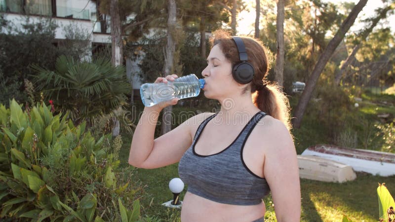 концепция спорта и фитнеса. кудрявая женщина, попивающая воду, во время пробежки на свежем воздухе