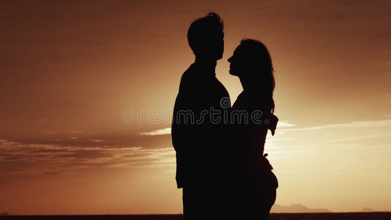 концерт. силуэт влюбленной пары держит за руки по вечерам на морском закате. мужчина показывает мечту пальцем