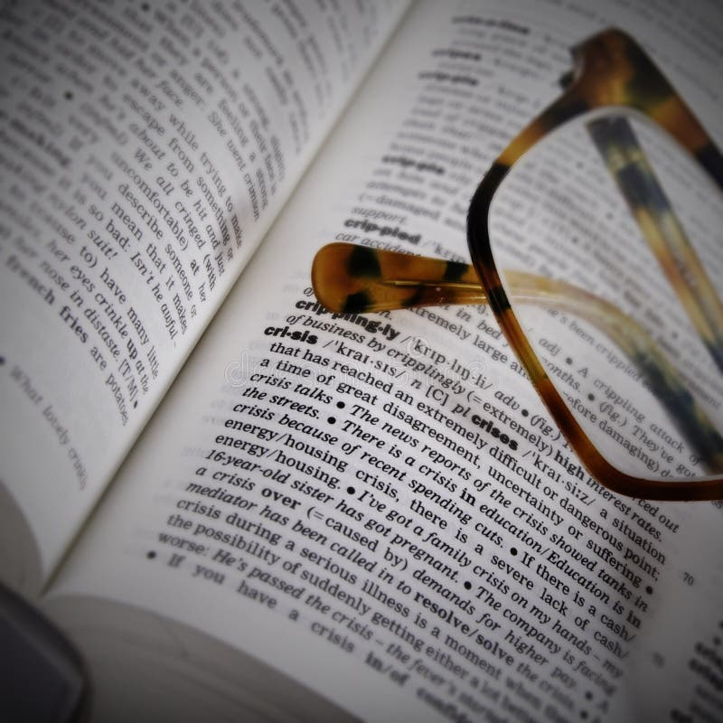 Dictionary page closeup with the word crisis and brown glasses on it. Dictionary page closeup with the word crisis and brown glasses on it