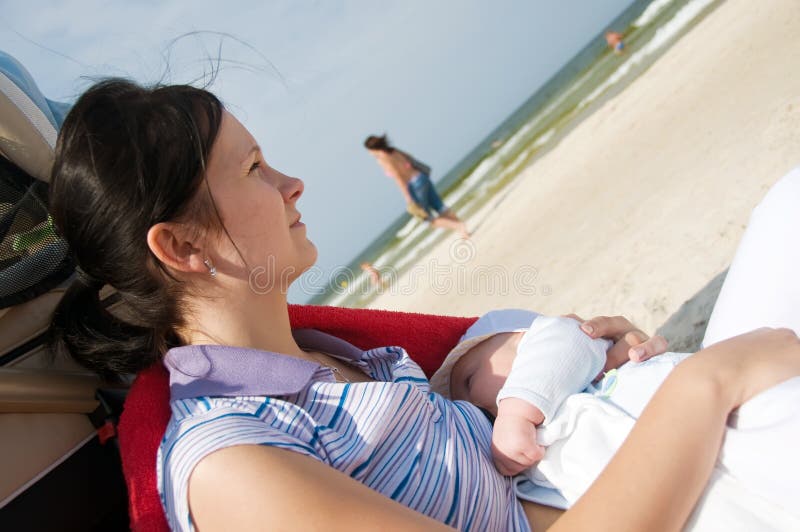 Thoughtful mother breast feeding her newborn on the beach. Thoughtful mother breast feeding her newborn on the beach.