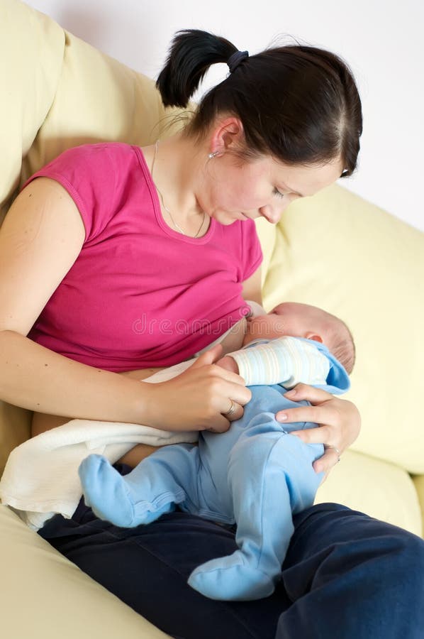 Mother breast feeding her newborn on sofa on mother's laps. Mother breast feeding her newborn on sofa on mother's laps.
