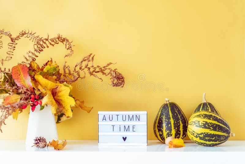 Коробка с текстом AUTUMN TIME, декоративные полосатые тыквы, ваза с букетом падающих листьев и паром на фоне золотой стены стоковые фотографии rf