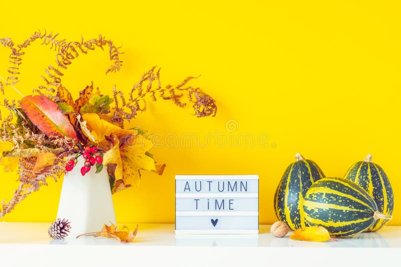Коробка с текстом AUTUMN TIME, декоративные полосатые тыквы, ваза с букетом падающих листьев и паром на ярко желтой стене стоковые изображения