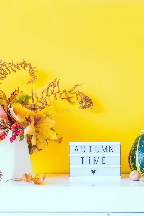 Коробка с текстом AUTUMN TIME, декоративные полосатые тыквы, ваза с букетом падающих листьев, паром на фоне желтой стены стоковая фотография rf