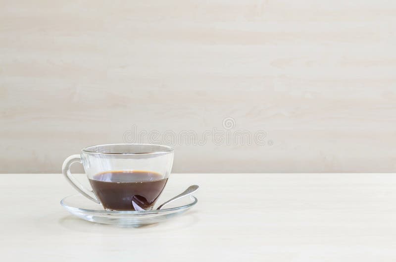 Black coffee in transparent cup of coffee on blurred wooden desk and wall textured background in the meeting room under window light. Black coffee in transparent cup of coffee on blurred wooden desk and wall textured background in the meeting room under window light