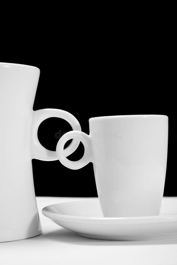 Two white coffee cups over a black background with overlapping handles. Two white coffee cups over a black background with overlapping handles