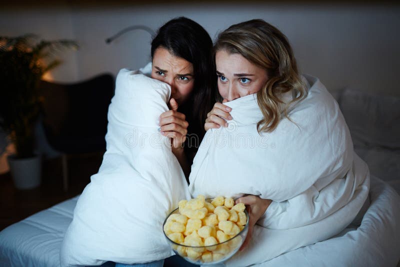 Scared girls hiding in blanket while watching horrors on TV at night. Scared girls hiding in blanket while watching horrors on TV at night