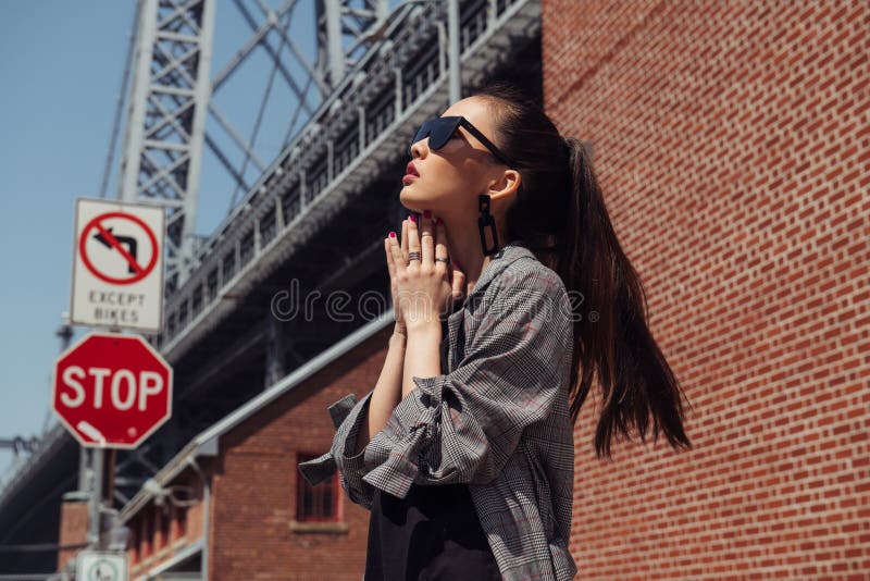 Красивая азиатская девушка фотомодели представляя на улице города нося стильные одежды и солнечные очки джинсовой ткани стоковые фотографии rf Красивая азиатская девушка фотомодели представляя на улице города нося стильные одежды и солнечные очки джинсовой ткани стоковые фотографии rf