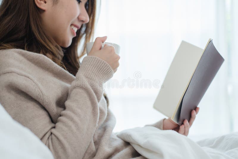 Красивая азиатская женщина наслаждаясь теплыми кофе и книгой чтения стоковое фото