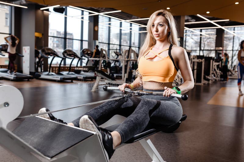 Красивая атлетическая девушка с длинными светлыми волосами одетыми в sportswear делает тренировки спорта с оборудованием на стоковое изображение Красивая атлетическая девушка с длинными светлыми волосами одетыми в sportswear делает тренировки спорта с оборудованием на стоковое изображение