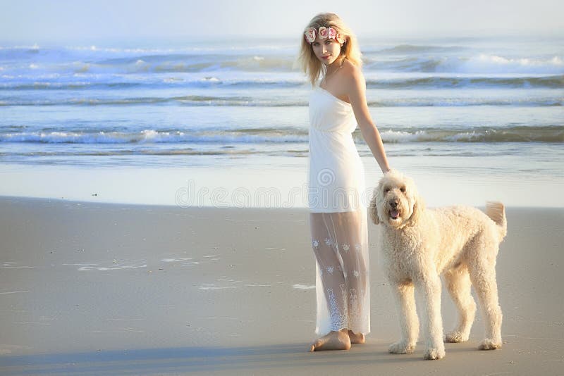 Красивая белокурая женщина на пляже в белом платье с ее собакой Goldendoodle стоковые изображения rf Красивая белокурая женщина на пляже в белом платье с ее собакой Goldendoodle стоковые изображения rf