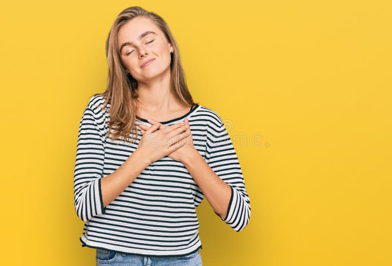 Beautiful blonde woman wearing casual clothes smiling with hands on chest with closed eyes and grateful gesture on face. health concept. Beautiful blonde woman wearing casual clothes smiling with hands on chest with closed eyes and grateful gesture on face. health concept