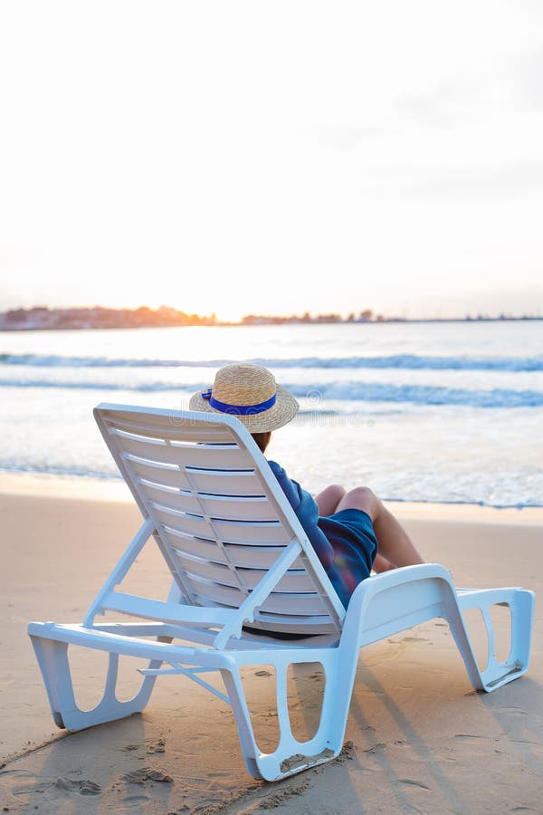 Красивая девушка в шляпе сидит на deckchair встречая рассвет стоковое фото rf Красивая девушка в шляпе сидит на deckchair встречая рассвет стоковое фото rf