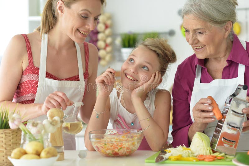 Красивая девушка с мамой и бабушкой готовя вкуснейший свежий салат стоковая фотография