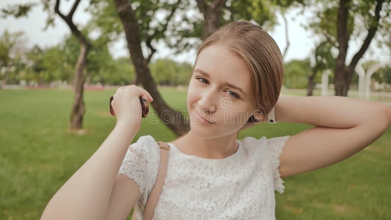 Красивая девушка студента, усмехаясь, расчесывает ее длинные волосы в парке Остатки во время исследования
