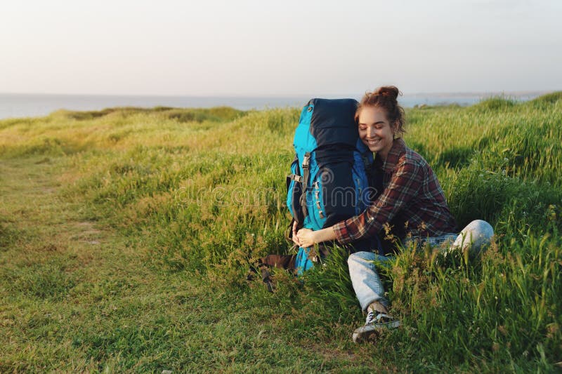 Красивая женщина hiker обнимая ее рюкзак в траве и усмехаться стоковые изображения