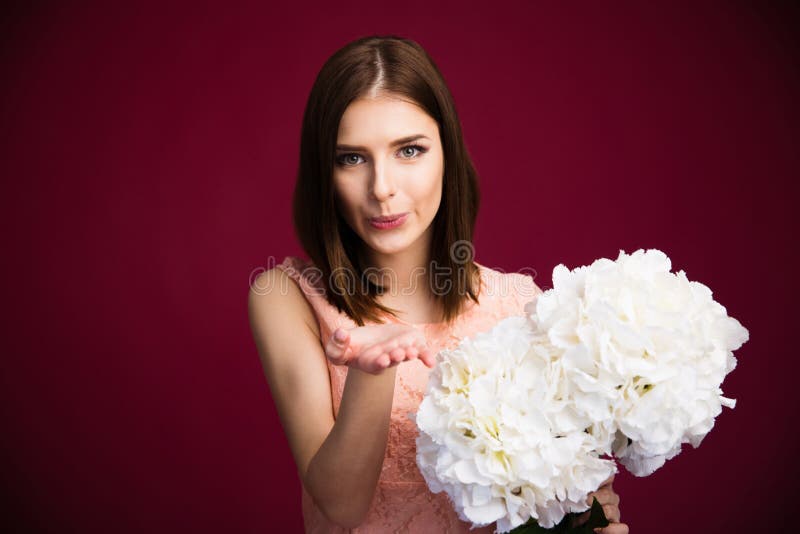 Beautiful woman holding flowers and sending kiss over pink background. Looking at camera. Beautiful woman holding flowers and sending kiss over pink background. Looking at camera