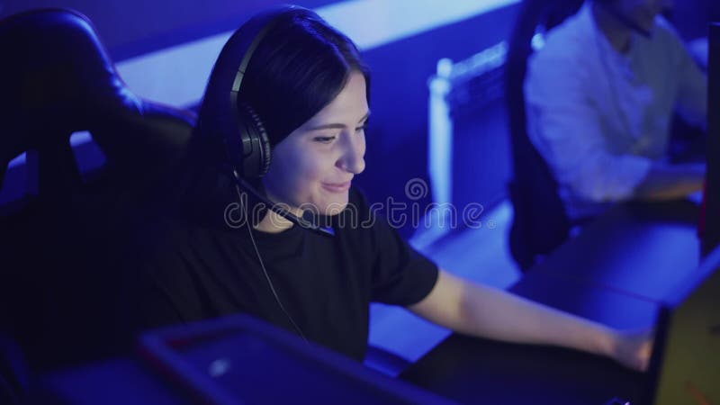 Красивая женщина играет Онлайн-игры в клубе компьютера. Молодая женщина сидит в наушниках и смеется совместно Игра