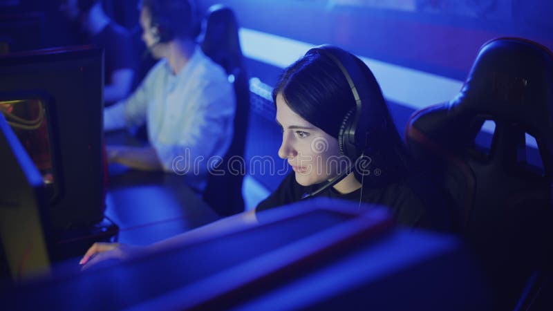 Красивая женщина играет Онлайн-игры в современном клубе компьютера. Молодая женщина сидит в наушниках перед монитором