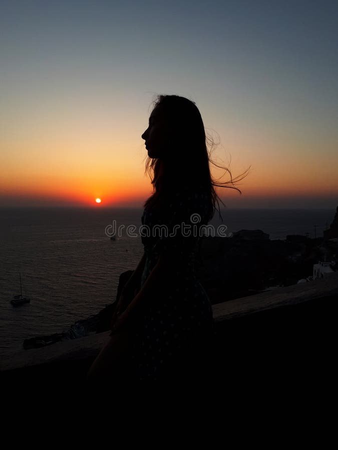 Красивая женщина наблюдая красочный оранжевый заход солнца в Oia, Santorini, Греции стоковое фото Красивая женщина наблюдая красочный оранжевый заход солнца в Oia, Santorini, Греции стоковое фото
