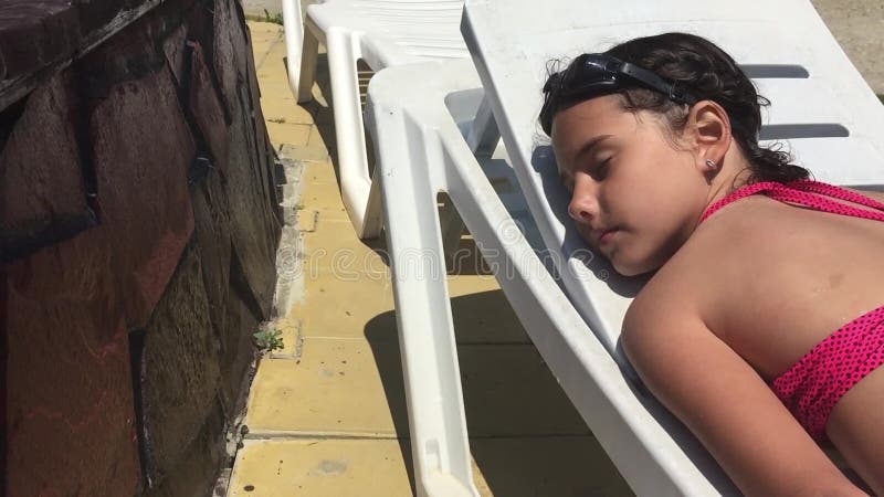 Beautiful little girl intended for teenagers in a swimsuit lies on a sun lounger near the pool and sleep video material - Video numbering sunny, swimsuit: 99617894   