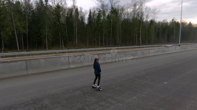 Красивая молодая женщина правит в одиночку на шоссе на hoverboard до заката