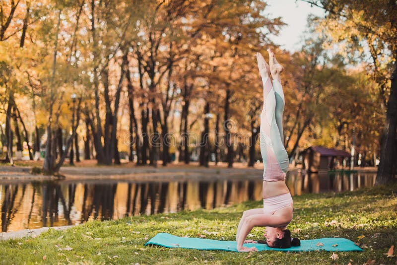 Красивая молодая женщина практикует asana йоги на деревянном столе в парке осени стоковые фотографии rf