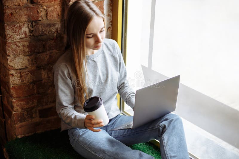 Красивая молодая женщина сидя на windowsill и используя компьтер-книжку стоковые изображения rf Красивая молодая женщина сидя на windowsill и используя компьтер-книжку стоковые изображения rf