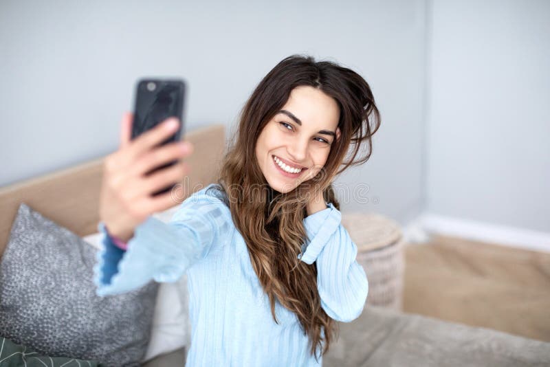Красивая молодая усмехаясь женщина с телефоном в ее руках принимает selfie стоковое фото Красивая молодая усмехаясь женщина с телефоном в ее руках принимает selfie стоковое фото