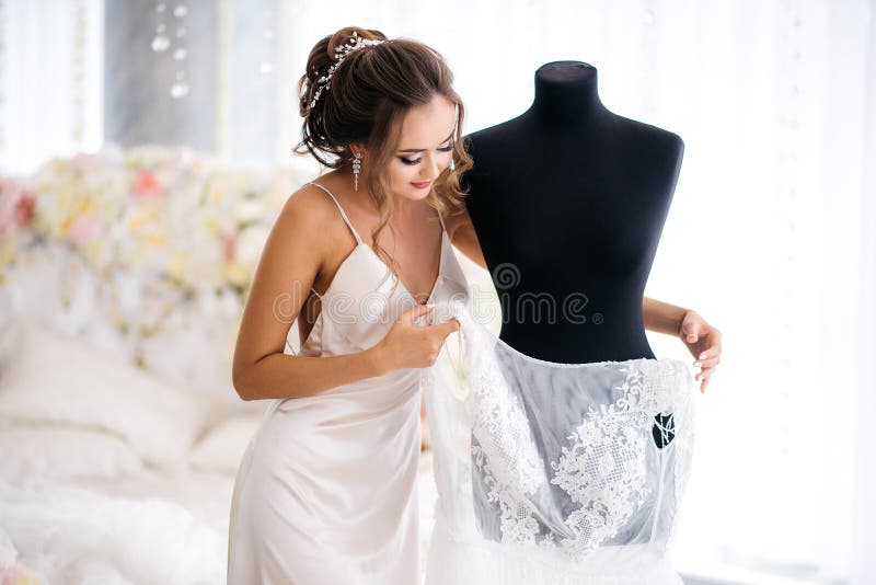 Красивая невеста в silk платье ночи принимает ее платье свадьбы от куклы в комнате будуара стоковое фото Красивая невеста в silk платье ночи принимает ее платье свадьбы от куклы в комнате будуара стоковое фото