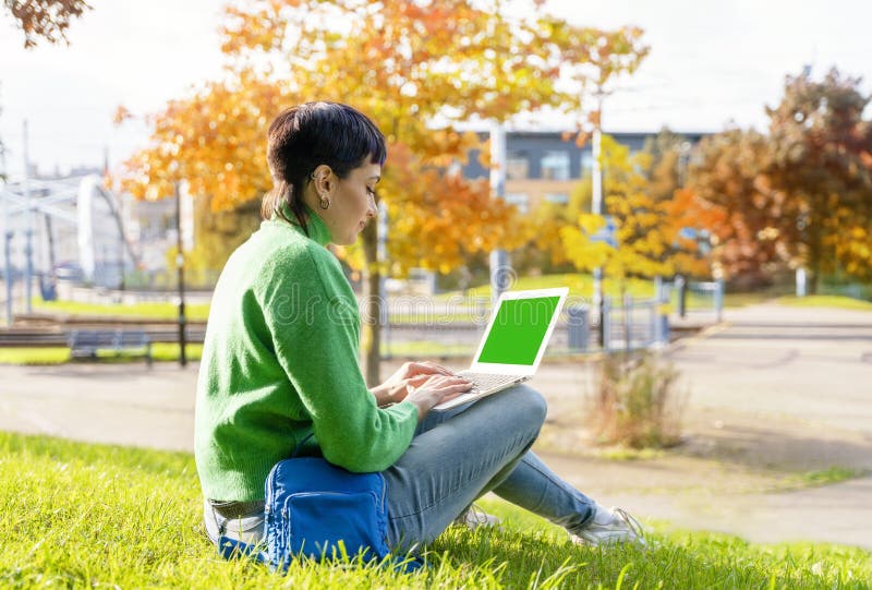 Portrait of a beautiful serious lady reading e-mails on the laptop while sitting in the city park. Portrait of a beautiful serious lady reading e-mails on the laptop while sitting in the city park