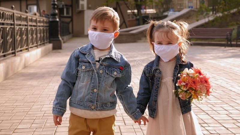 Красивые маленькие ребенка маски в медицинские в парке, девушка с букетом цветов