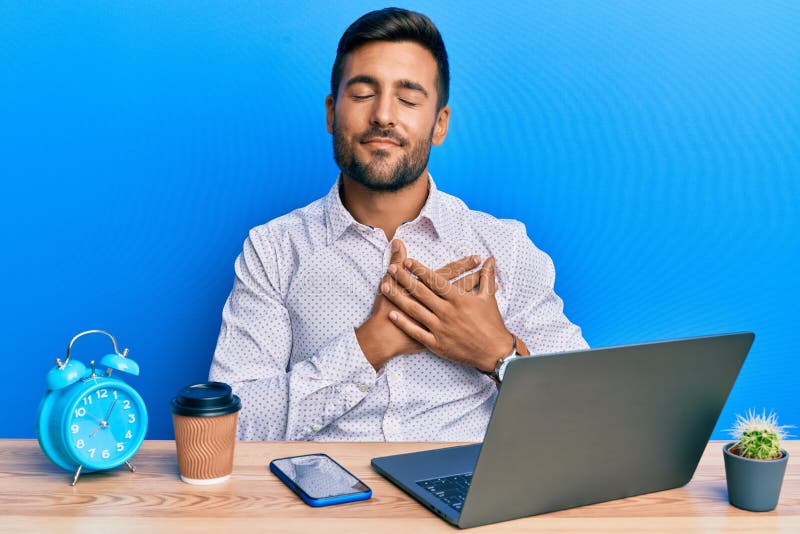Handsome hispanic man working using laptop at the office smiling with hands on chest, eyes closed with grateful gesture on face. health concept. Handsome hispanic man working using laptop at the office smiling with hands on chest, eyes closed with grateful gesture on face. health concept