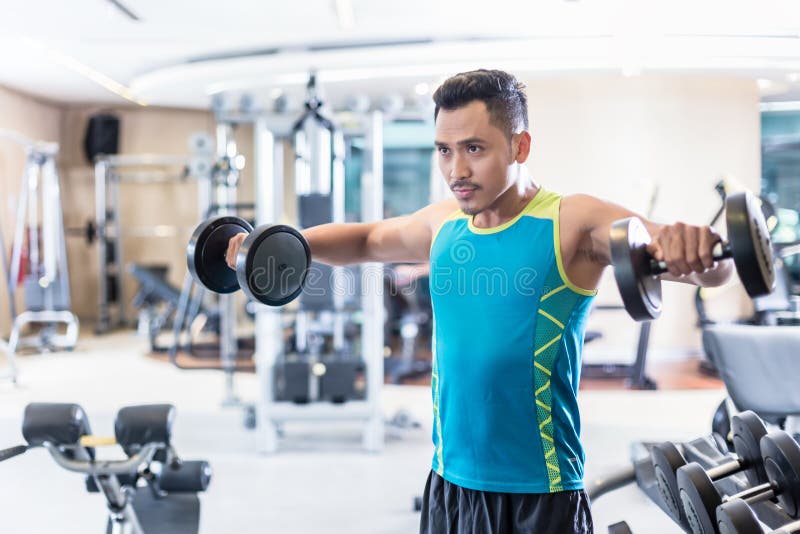 Portrait of a handsome determined young man exercising with dumbbells during upper-body workout routine in a modern fitness club. Portrait of a handsome determined young man exercising with dumbbells during upper-body workout routine in a modern fitness club