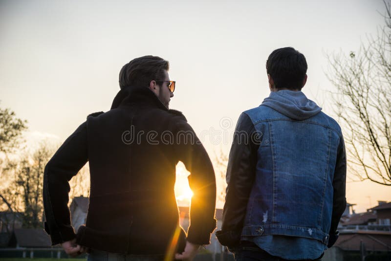 Two handsome casual trendy young men, 2 friends, in an urban park walking and chatting together. Two handsome casual trendy young men, 2 friends, in an urban park walking and chatting together
