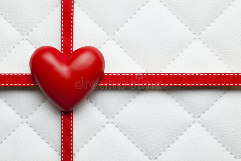 Red heart and red ribbon on white quilted leather background. Red heart and red ribbon on white quilted leather background