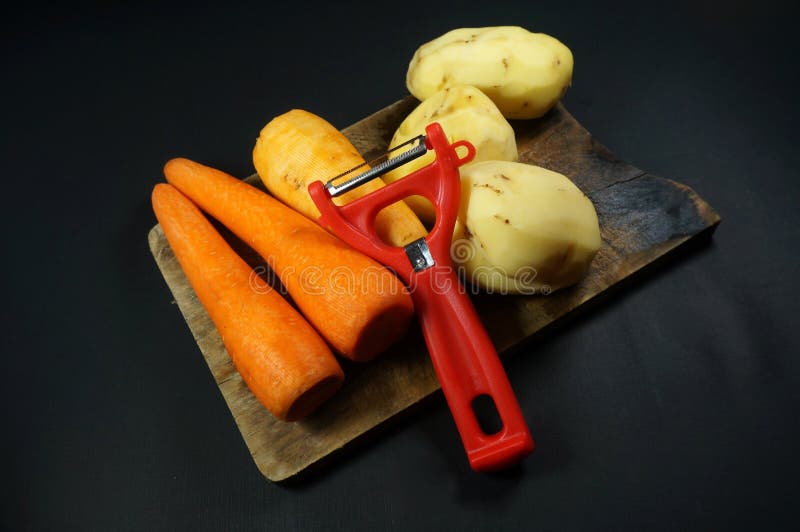Красный peeler с очищенный морковь и картофелем изолированными на фоне darkblack. Выборочный фокус. Минималистский и плоская концепция. Вид сверху.