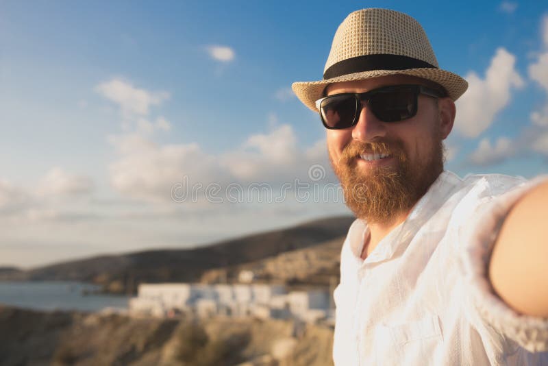 Красный бородатый путешественник битника в солнечных очках и шляпе делает selfie на каникулах на предпосылке seashore стоковые изображения rf Красный бородатый путешественник битника в солнечных очках и шляпе делает selfie на каникулах на предпосылке seashore стоковые изображения rf