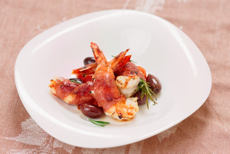 Shrimps with bacon, olives and rosemary in plate on table. Shrimps with bacon, olives and rosemary in plate on table