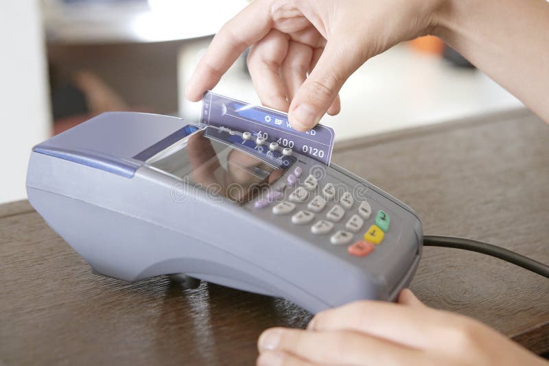 Close up of a store attendant's hand sweeping a credit card in a card reader at a shop counter. Close up of a store attendant's hand sweeping a credit card in a card reader at a shop counter.