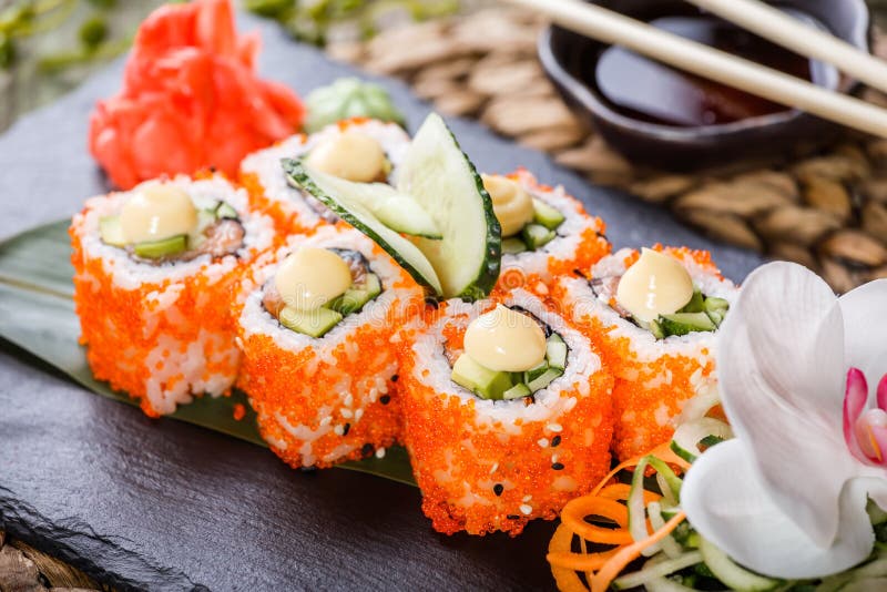 Крен суш - суши Maki сделанные из семг, красного плавленого сыра икры, огурца, авокадоа и на черном камне на бамбуковой циновке у стоковая фотография Крен суш - суши Maki сделанные из семг, красного плавленого сыра икры, огурца, авокадоа и на черном камне на бамбуковой циновке у стоковая фотография