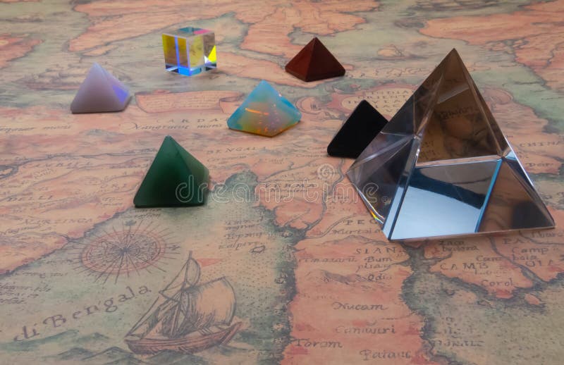 Кристаллическое pyramide и небольшие пирамиды естественных драгоценных камней со светлым кубом на карте античного мира стоковая фотография Кристаллическое pyramide и небольшие пирамиды естественных драгоценных камней со светлым кубом на карте античного мира стоковая фотография