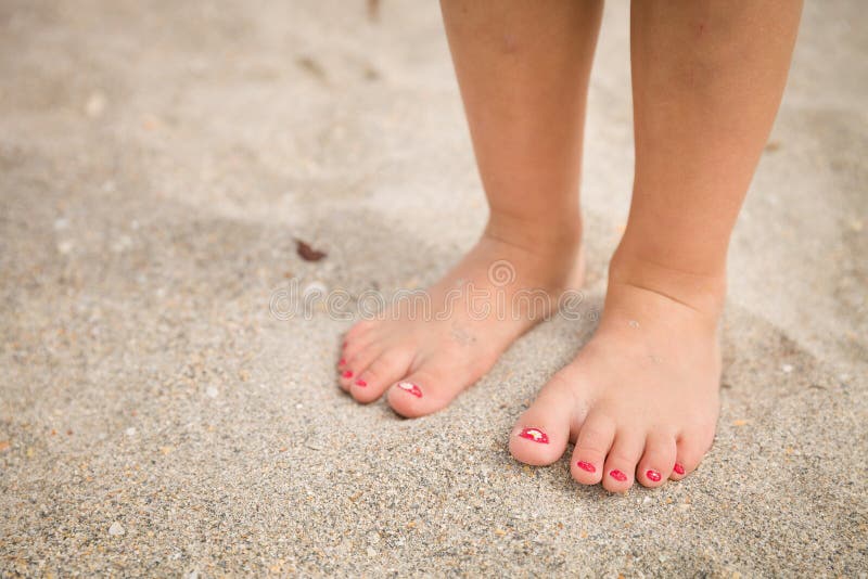 Closeup of a little girl`s legs and feet walking on the sand of the beach with the sea water in the background summer. Closeup of a little girl`s legs and feet walking on the sand of the beach with the sea water in the background summer.