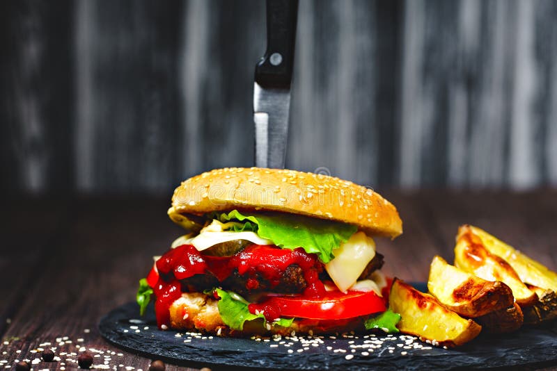 Крупный план рт-мочить, очень вкусные домодельные бургеры с ножом вставил на каменной доске деревянное предпосылки темное стоковые изображения Крупный план рт-мочить, очень вкусные домодельные бургеры с ножом вставил на каменной доске деревянное предпосылки темное стоковые изображения